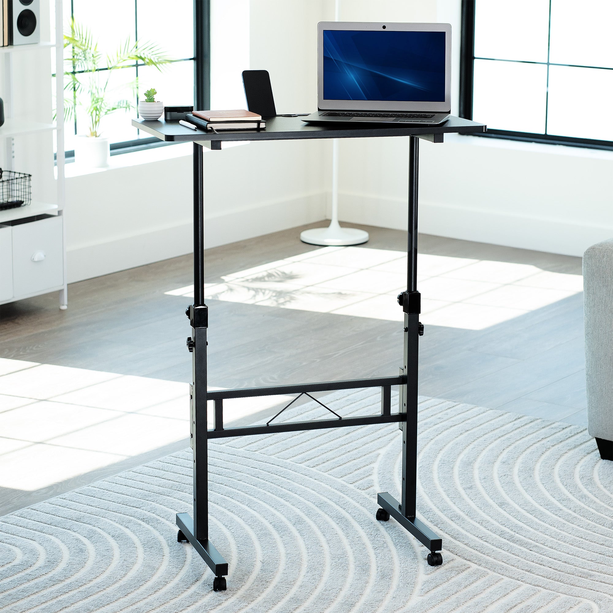 Portable desk with a laptop on a rug in a room with large windows