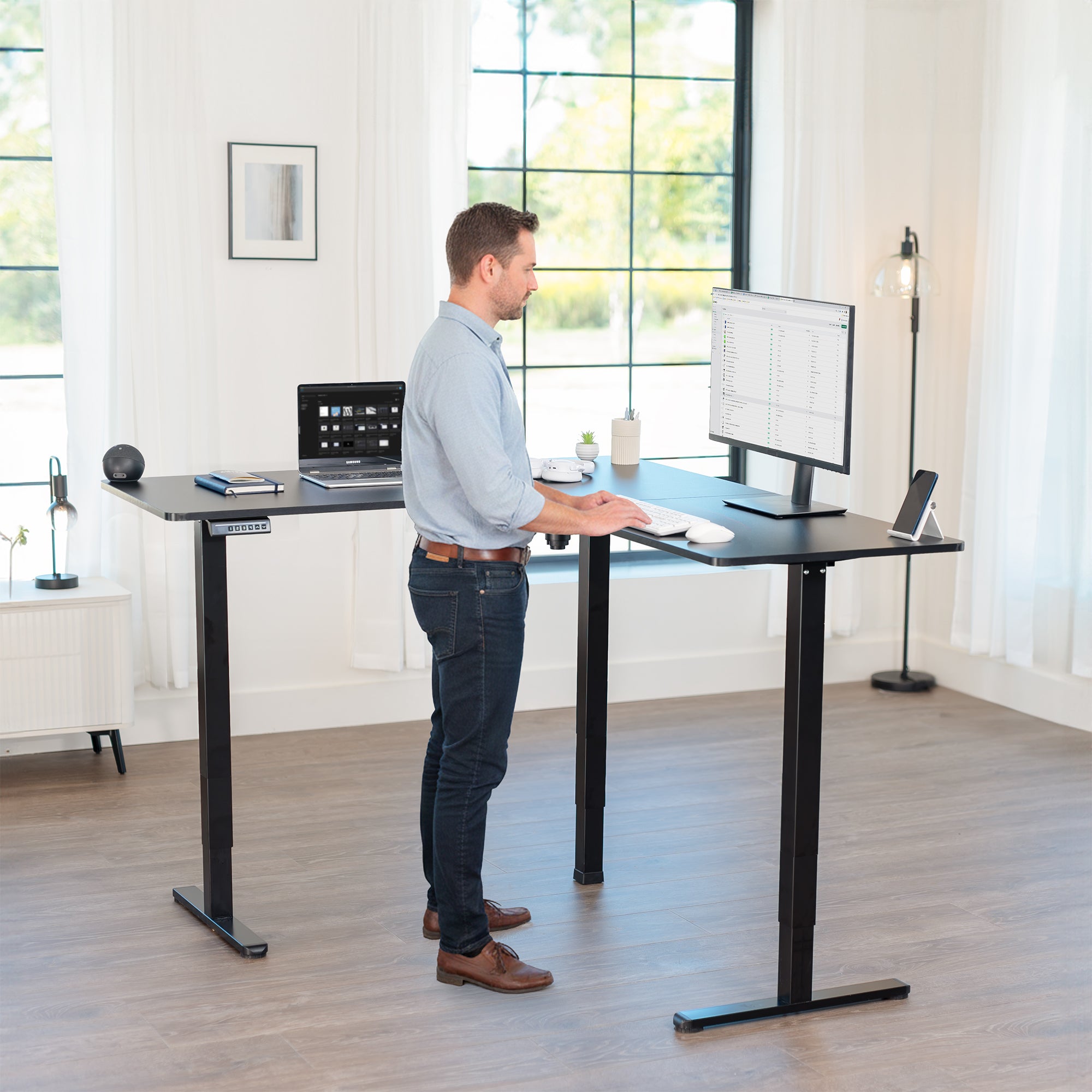 Man using a standing desk in a bright room with large windows.