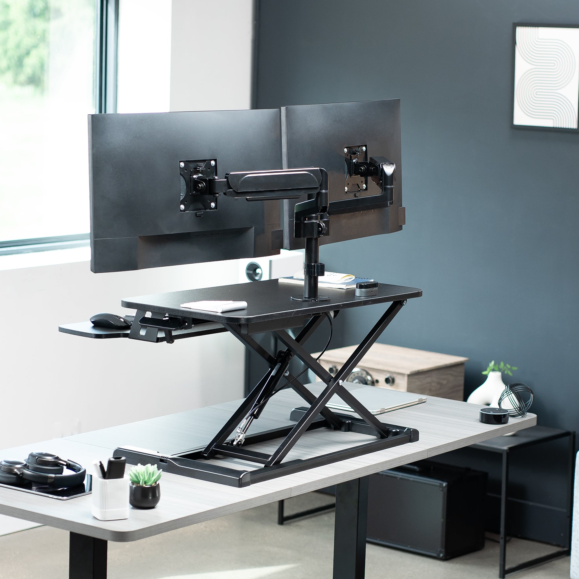 Height adjustable desk riser with articulating mechanical dual monitor mount.