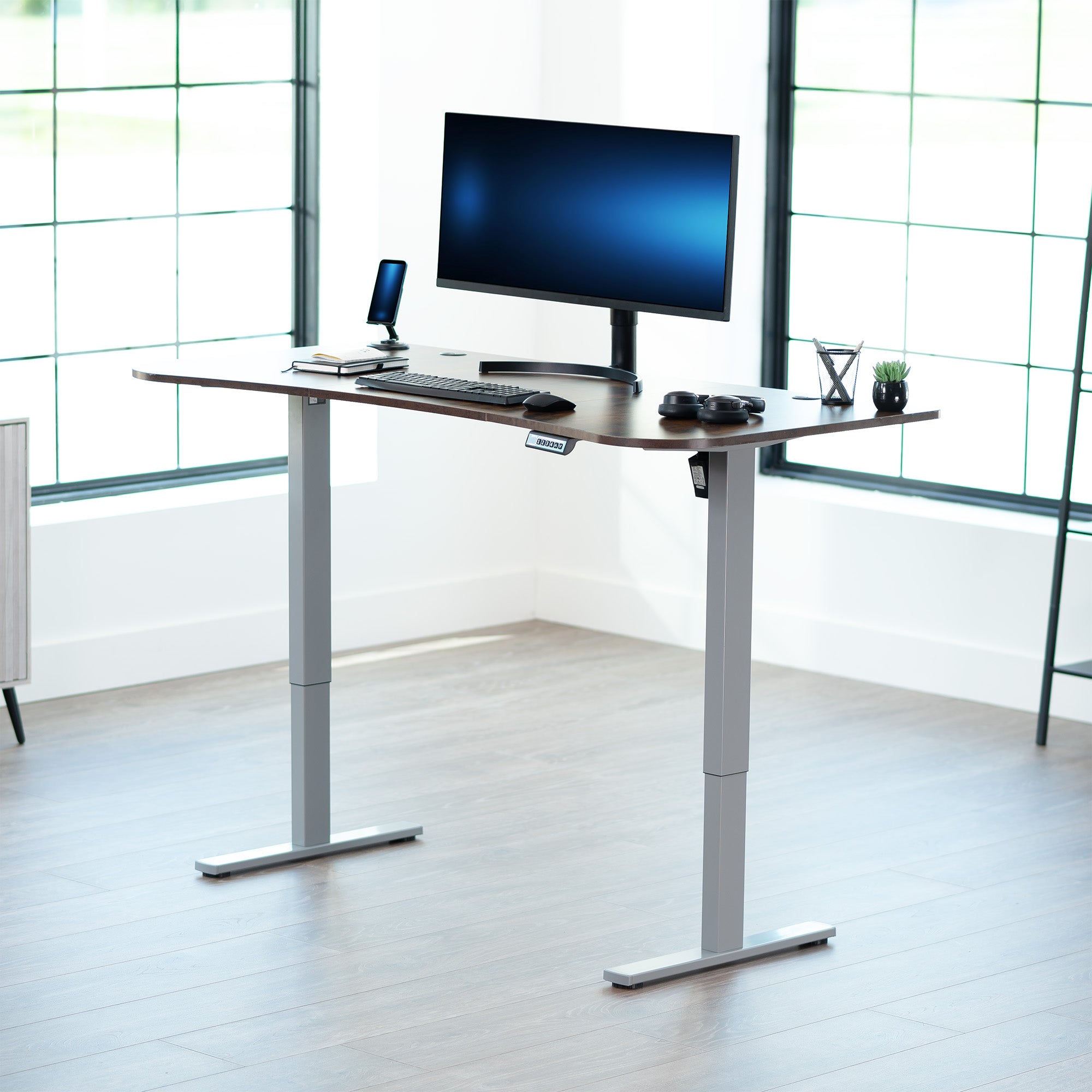 Rustic, vintage brown top grey frame, electric, sit to stand, height adjustable desk in office setting.