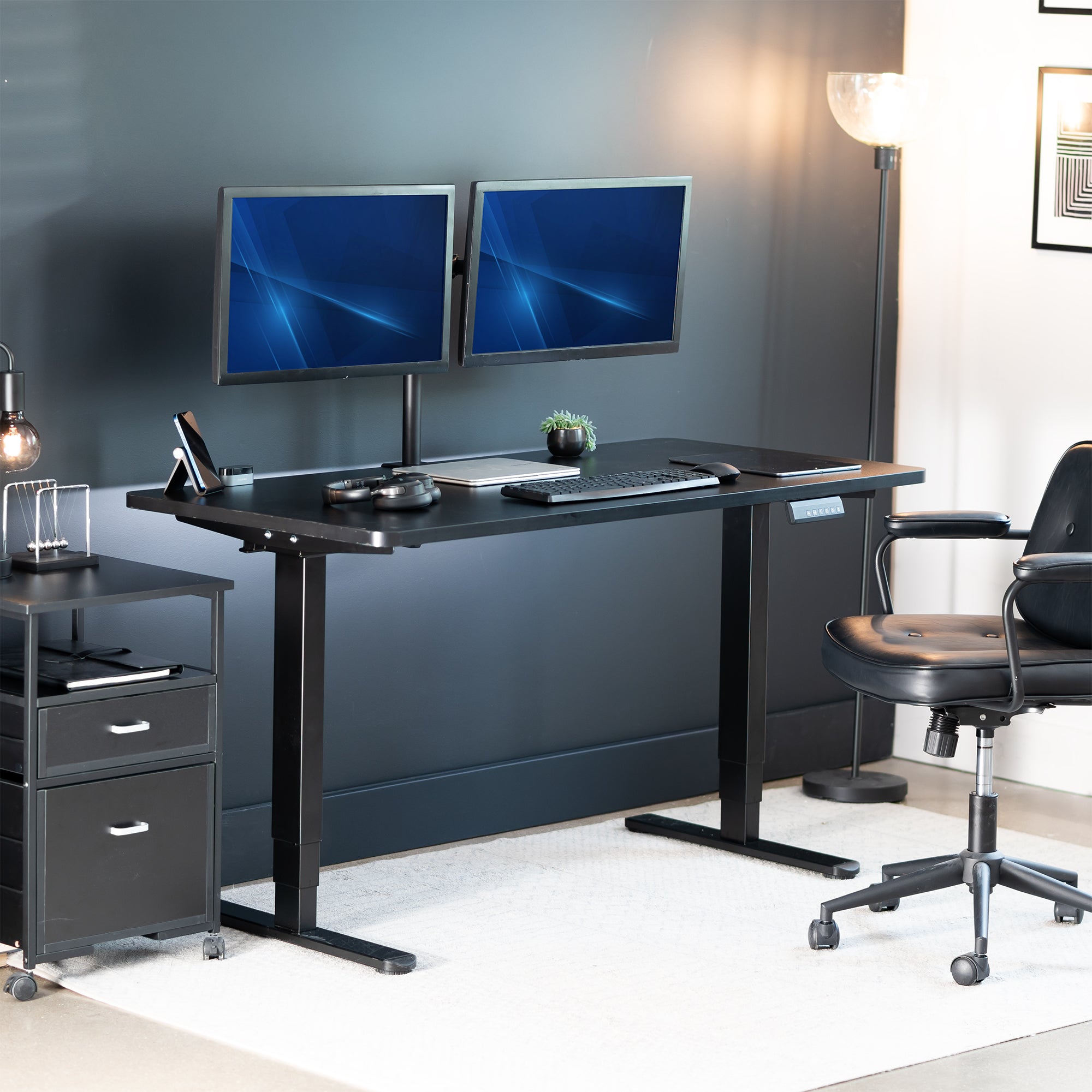 Modern office setup with a black desk, two monitors, a chair, and a lamp.