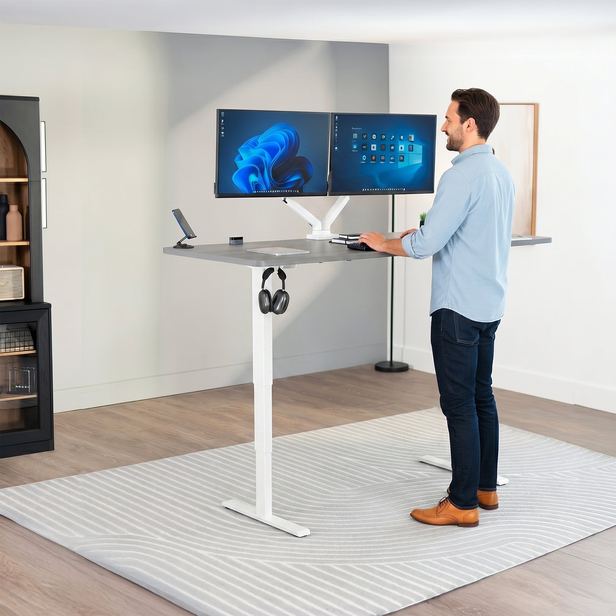 Man standing at an electric height adjustable desktop workstation in office space.