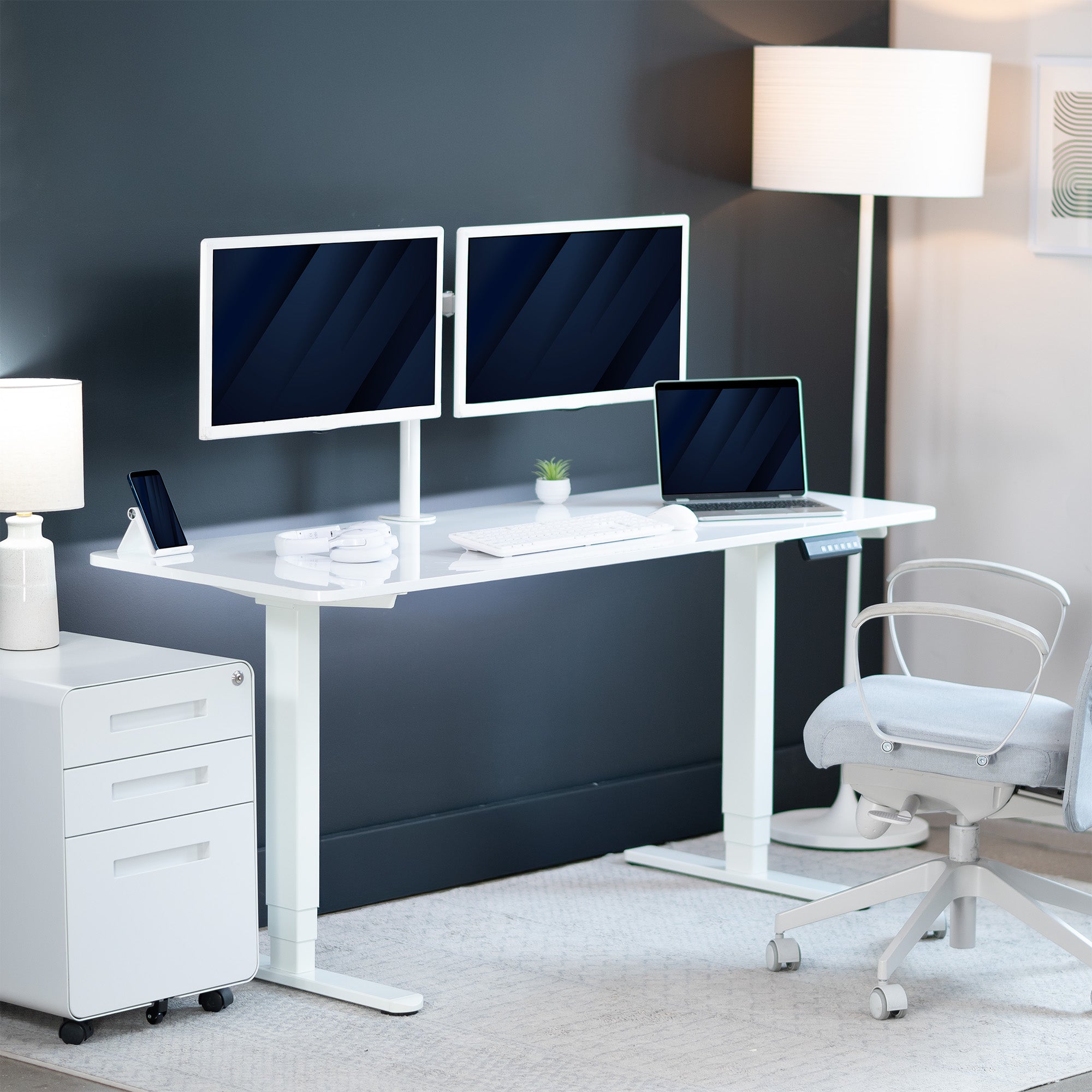 Modern office setup with a white desk, two monitors, a laptop, and office chair.