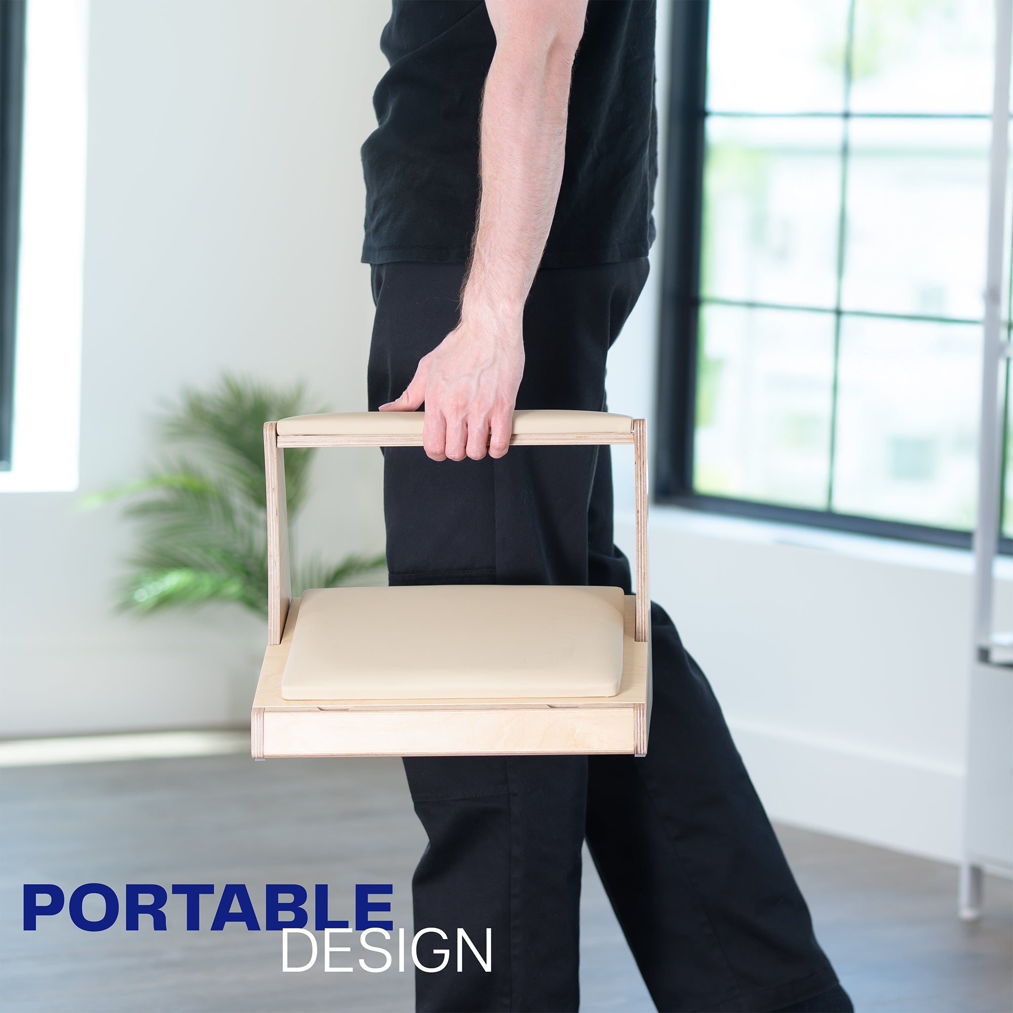 Person holding a portable wooden footrest in a minimalistic room.