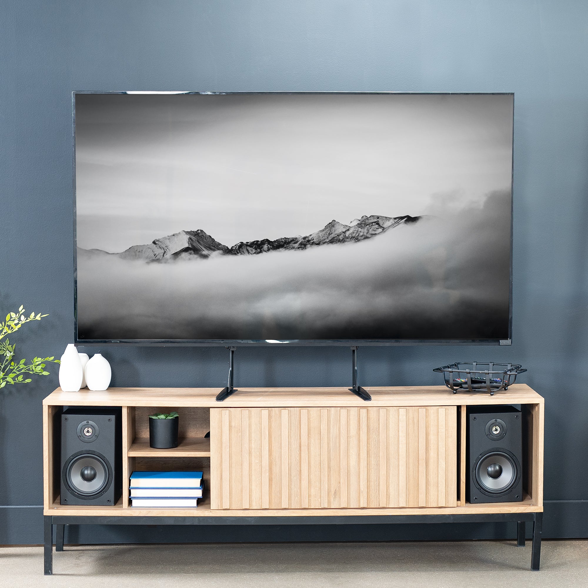 Steel TV stand with a large flat-screen TV displaying a mountain landscape against a blue wall.