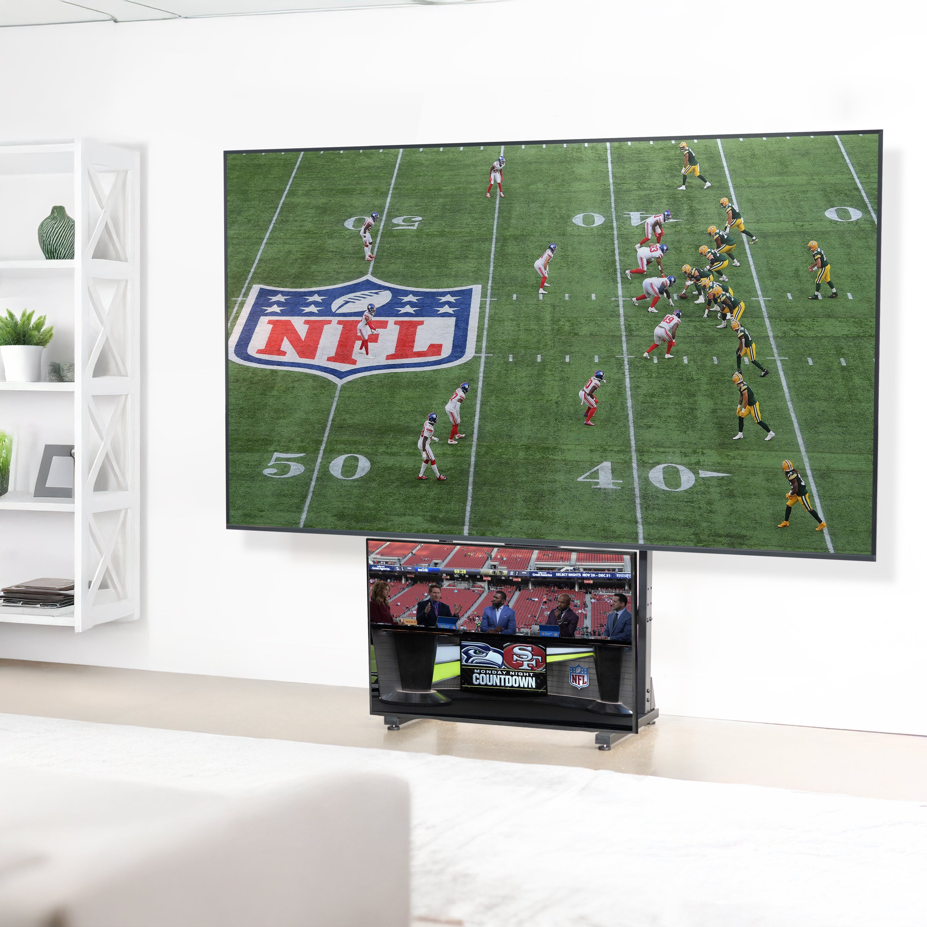 A large flat-screen television mounted on a heavy-duty floor stand with a football game on the screen.