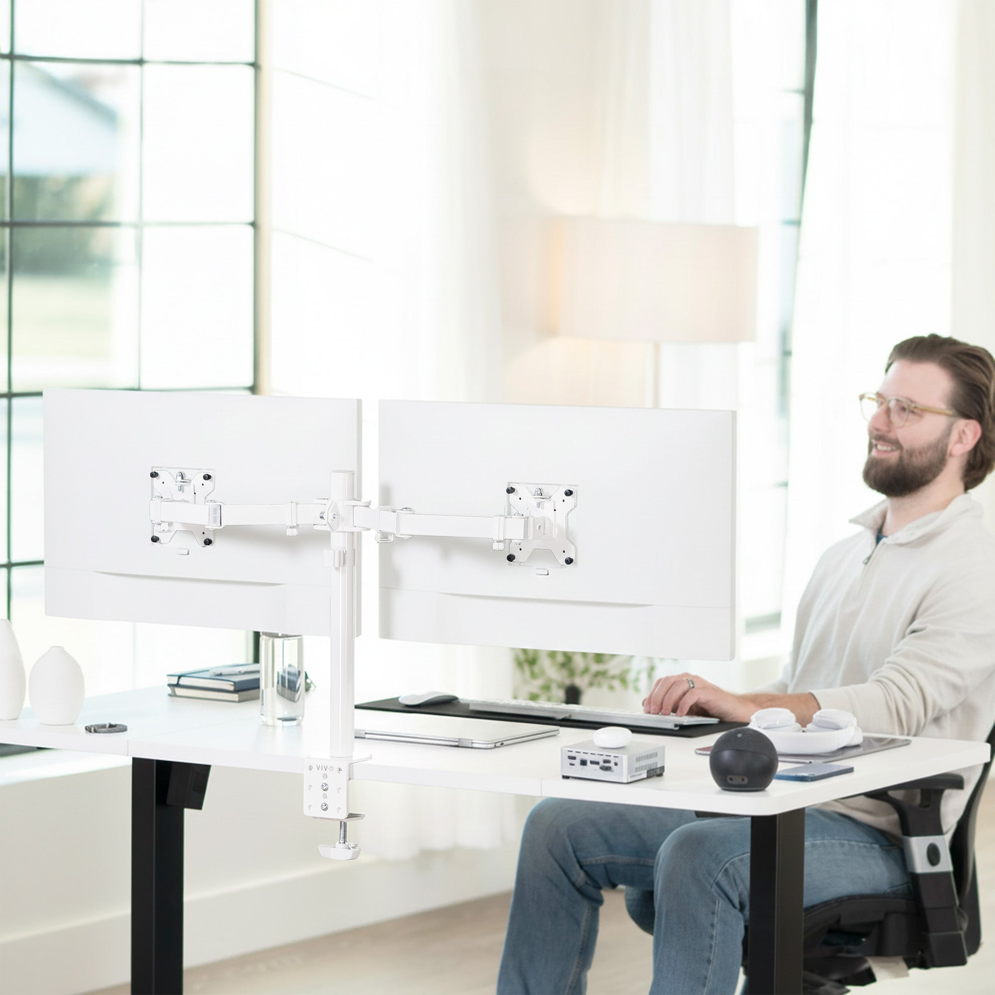 Man sitting at a modern desk with dual monitors attached to dual monitor desk mount in a bright office setting