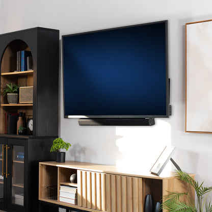 Modern living room with a flat-screen TV mounted on the wall with a  Soundbar TV Mount, wooden entertainment console, and bookshelf.
