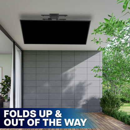 A TV mounted on a ceiling, shown folded down in an outdoor patio setting with a tiled wall, wooden deck, and green trees. A blue banner at the bottom reads 'FOLDS UP & OUT OF THE WAY'.