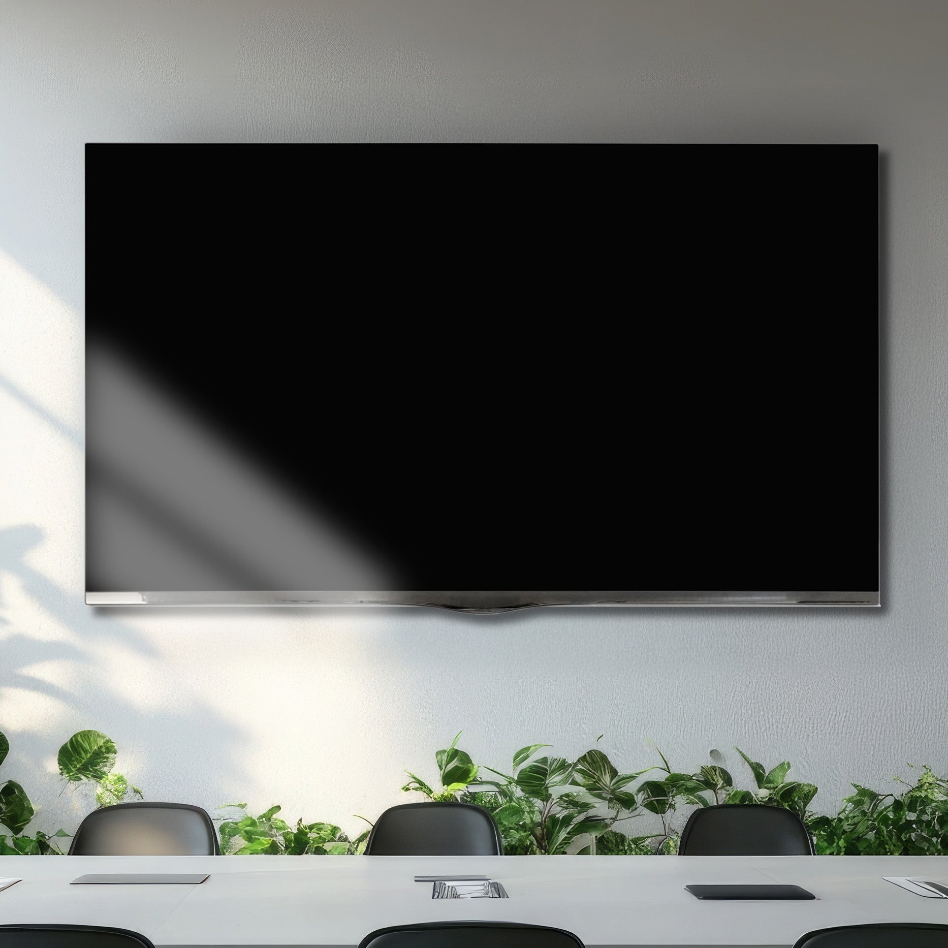 Large black screen TV mounted on a wall in a modern office setting with plants and chairs.