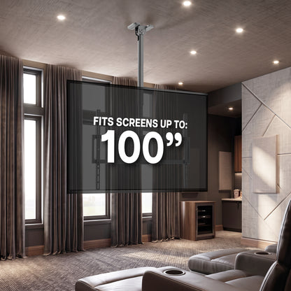 A large TV screen mounted on a ceiling in a modern home theater, with text overlay reading 'FITS SCREENS UP TO: 100"'. The room features gray leather recliners, brown curtains, and textured walls.