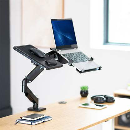 Adjustable desk stand with laptop, mouse, and phone on a wooden desk.