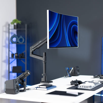 Modern office setup with a curved monitor on a Pneumatic Arm Single Ultrawide Monitor Desk Mount, featuring a dark gray wall and shelves in the background.