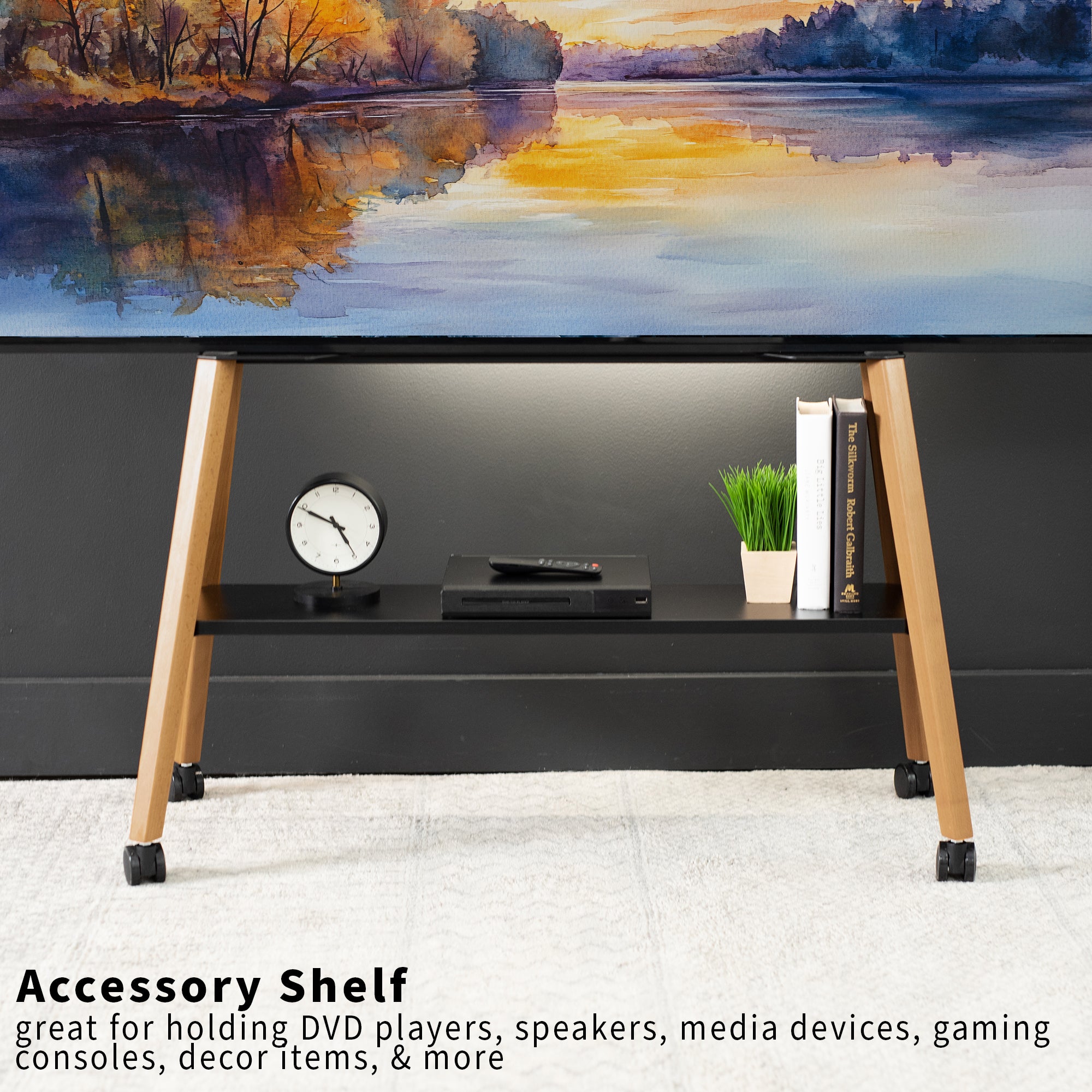 A black accessory shelf with walnut wood legs and black casters, shown holding a console, books, and a small plant in a room setting under a landscape painting.