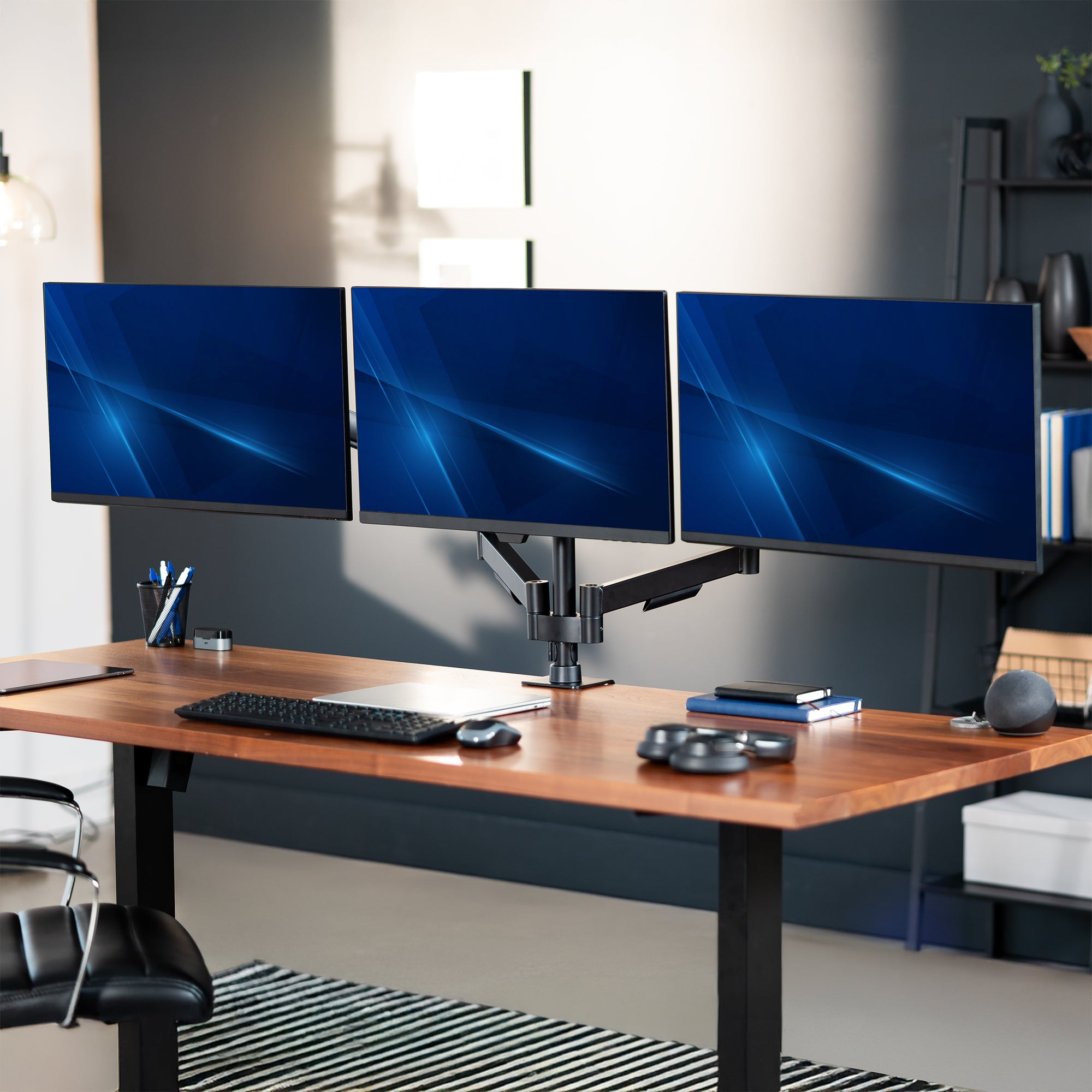 Three computer monitors on a desk in an office setting.
