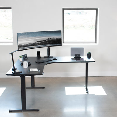 Lowered sit-to-stand office desk by windows with large monitor displayed.