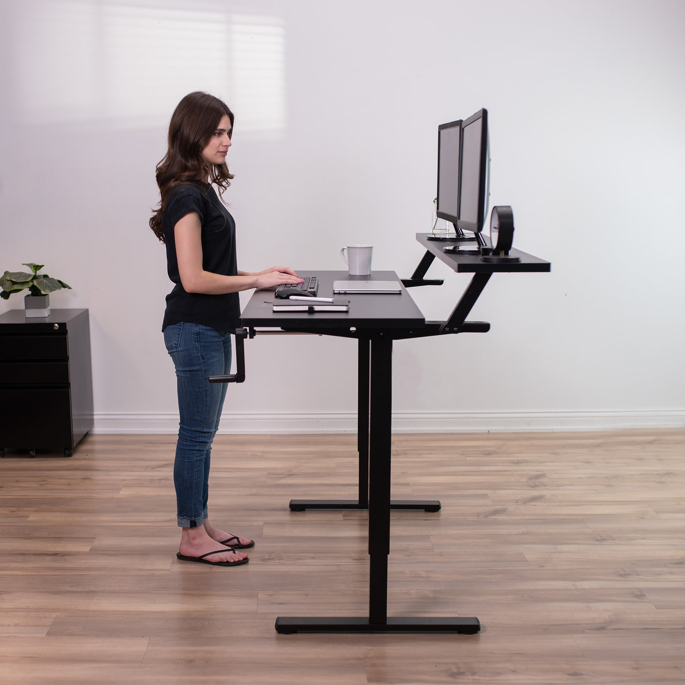 Woman working at an ergonomic height-adjustable split-top desk with elevated monitors.