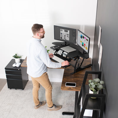 Live action office space with a sit-to-stand desk converter on an L-shaped desk.