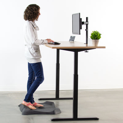 Woman standing while working at a modern sit-to-stand workstation desk from VIVO.