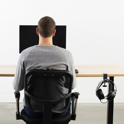 A man working at an office desk setup with headphones conveniently stored on the side of his desk.