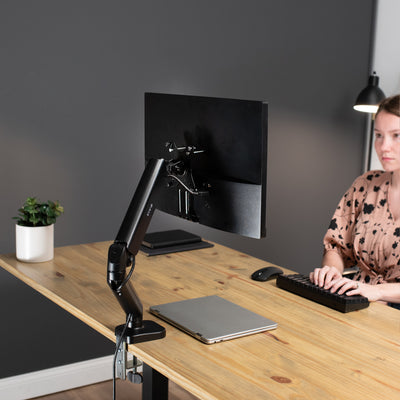 A woman working in an ergonomic office space with a monitor mounted by the help of an additional VESA adapter bracket from VIVO.