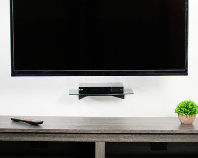 A large TV mounted above a wall mount glass shelf supporting an LG TV player.