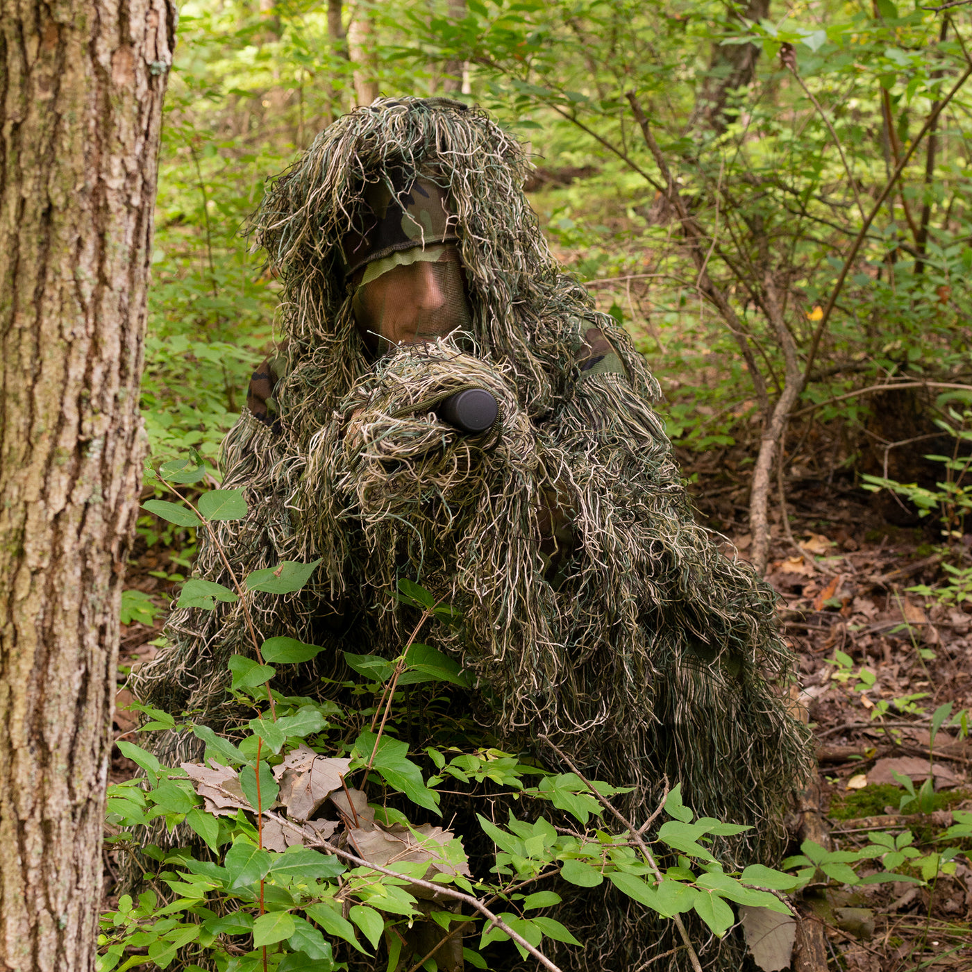 Man in a ghillie suit blending into the outdoor environment.