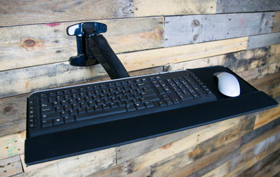 Steel keyboard tray mounted to a rustic wood wall.