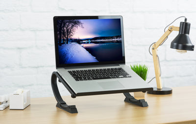 A desktop laptop stand with a plant, lamp, and other office supplies.